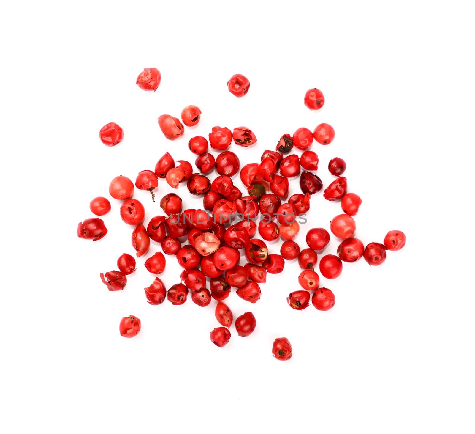 Close up heap of red pink pepper peppercorns spilled and spread around isolated on white background, elevated top view, directly above