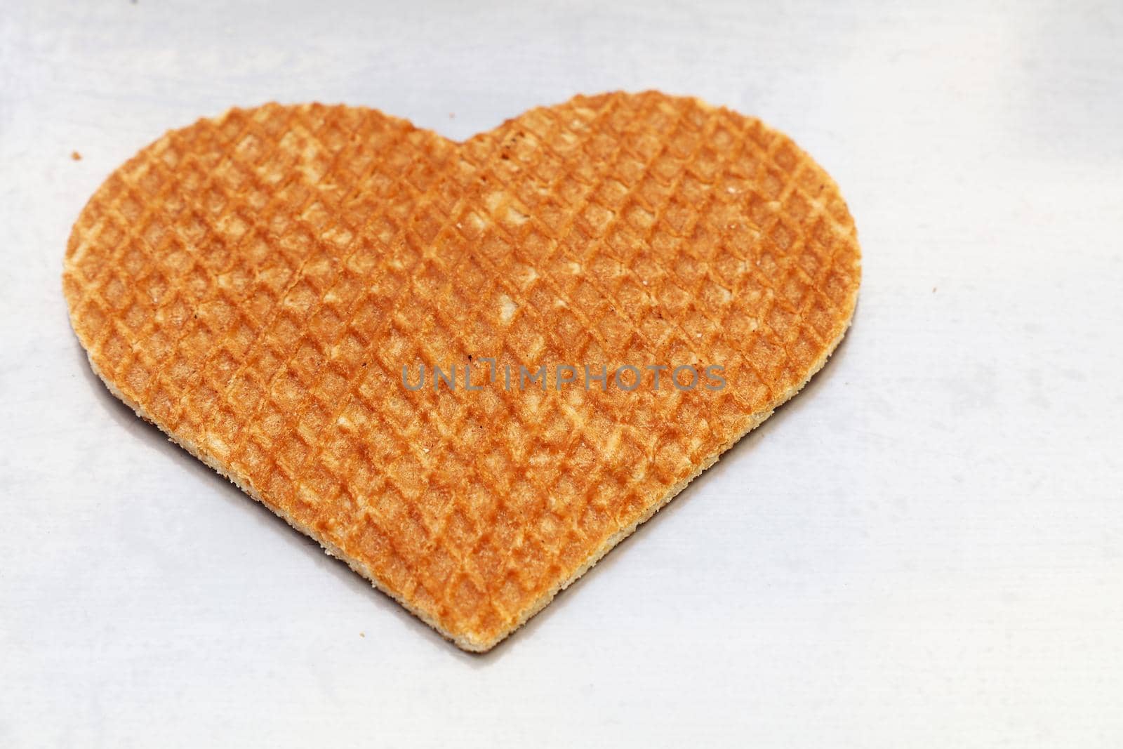 Close up one heart shaped traditional sweet Dutch stroopwafel (syrup waffle) cookie on white baking paper, high angle view