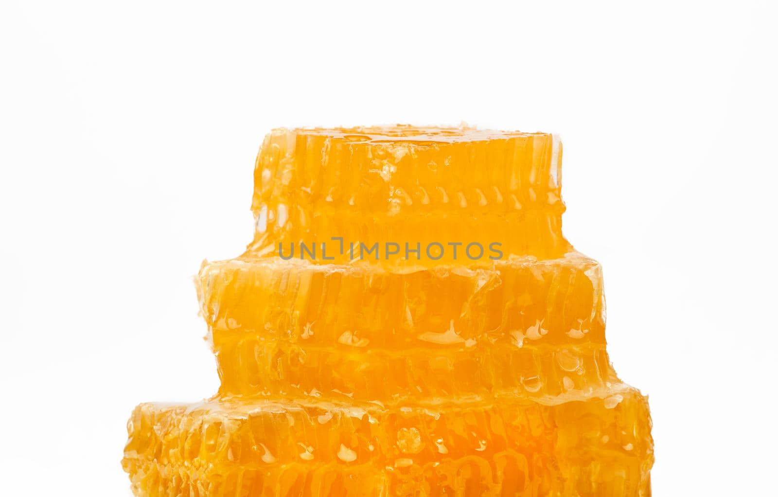 Close up stack of several fresh cut golden comb honey slices on plate isolated on white background, low angle, side view