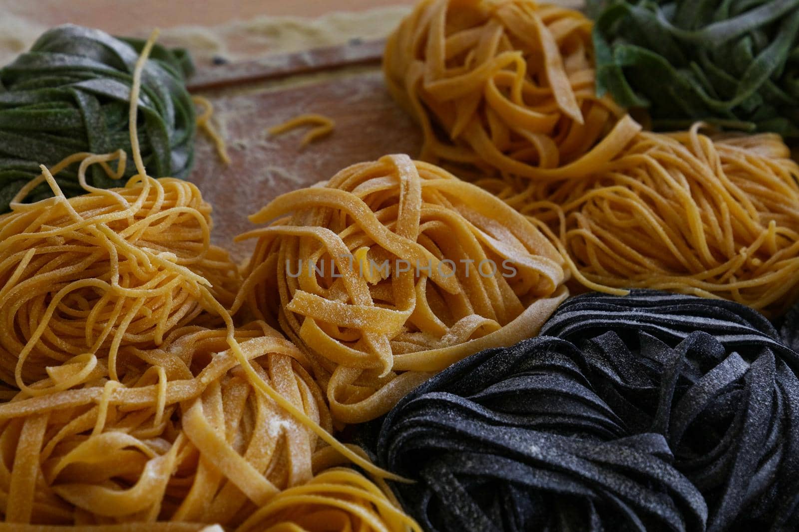 Close up cooking fresh handmade traditional Italian tagliatelle pasta, uncooked black, green and classical past on wooden table, high angle view