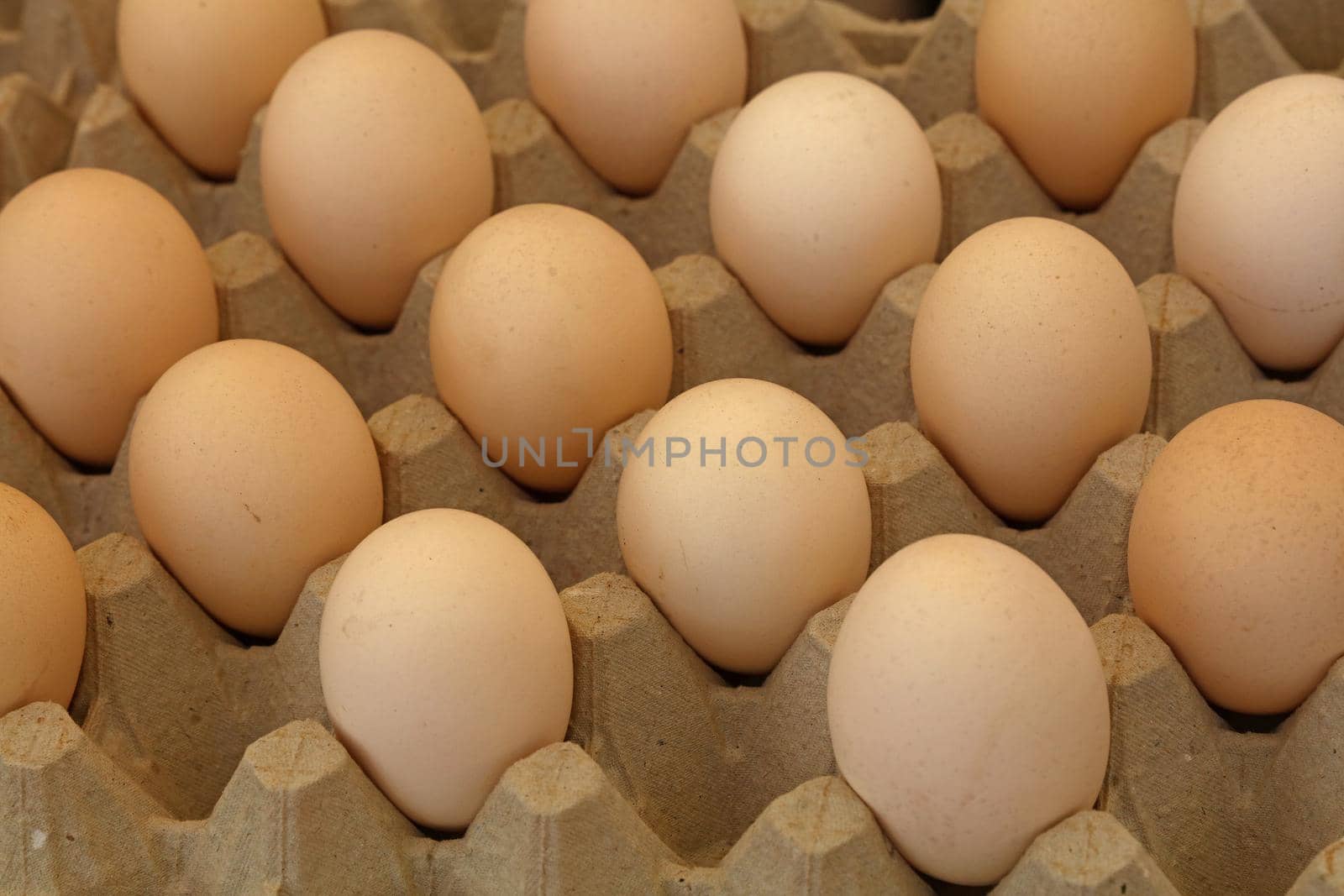 Close up many fresh brown chicken eggs in tray carton at retail display of farmers market, high angle view
