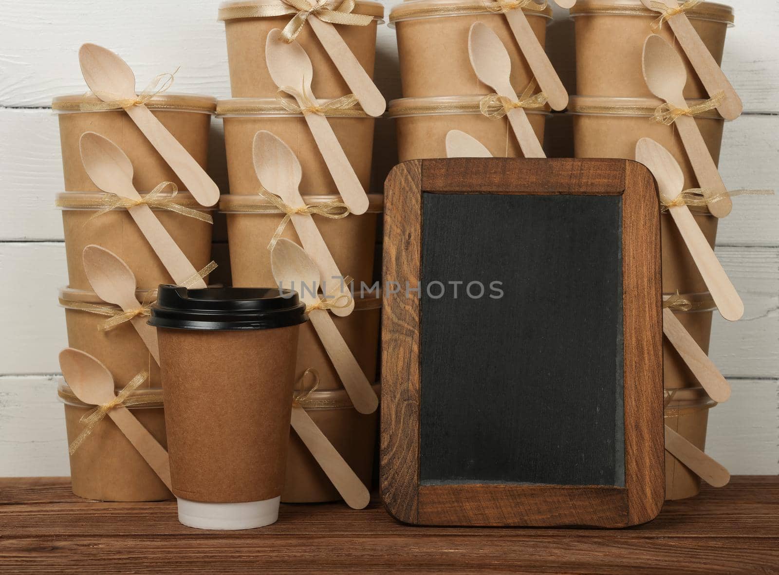 Close up brown paper coffee cup and empty blank black slate chalkboard sign over stack of desserts at coffee shop retail display