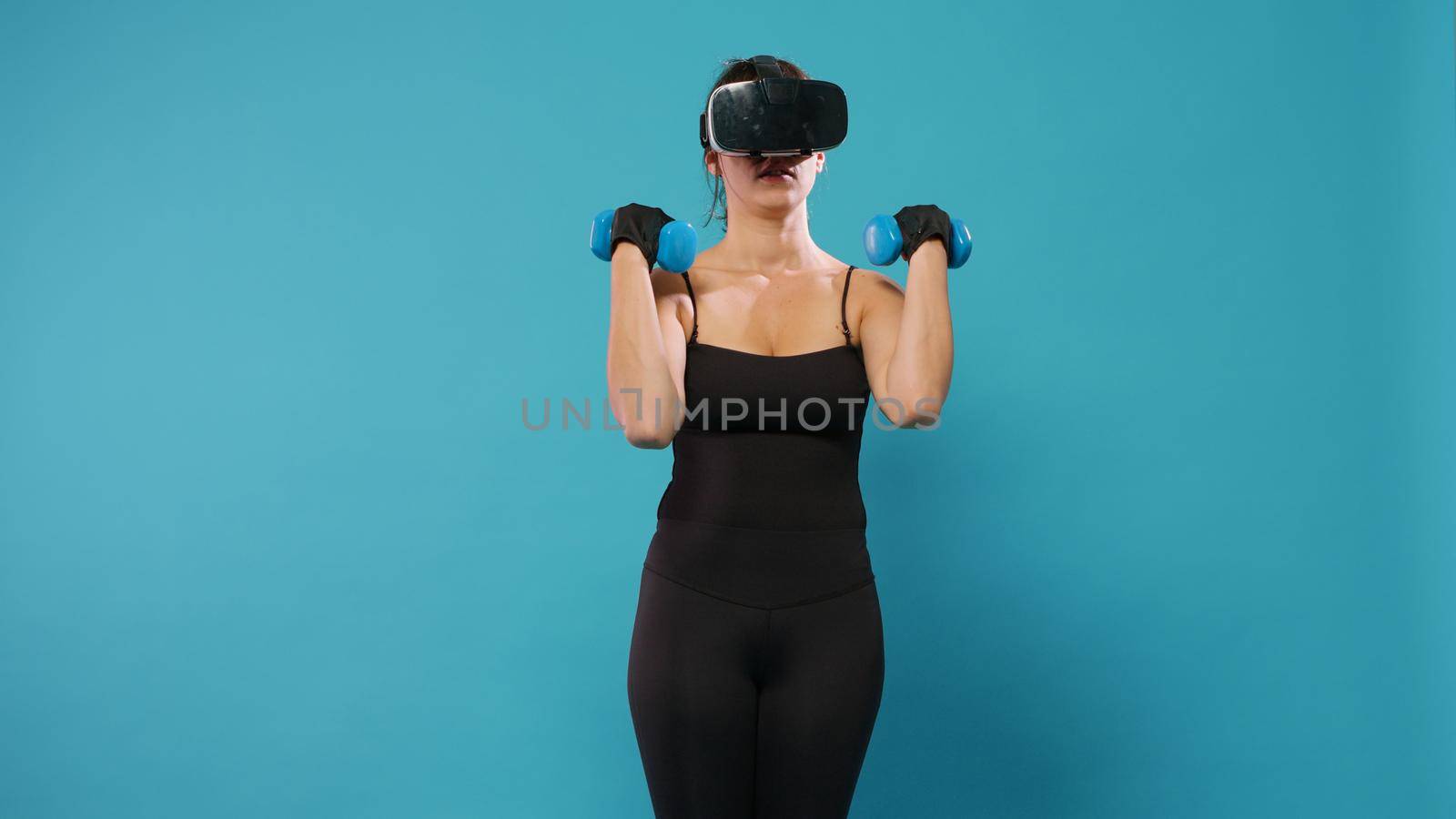 Athlete doing workout training with dumbbells and vr glasses, exercising in virtual reality. Fit woman wearing virtual reality headset to do fitness activity and train muscles with weights lifting