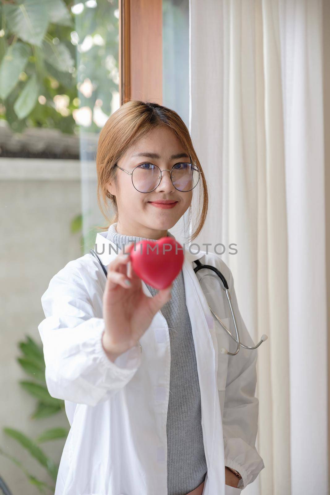Portrait young asian beautiful doctor with stethoscope holding heart while standing at her office. by nateemee