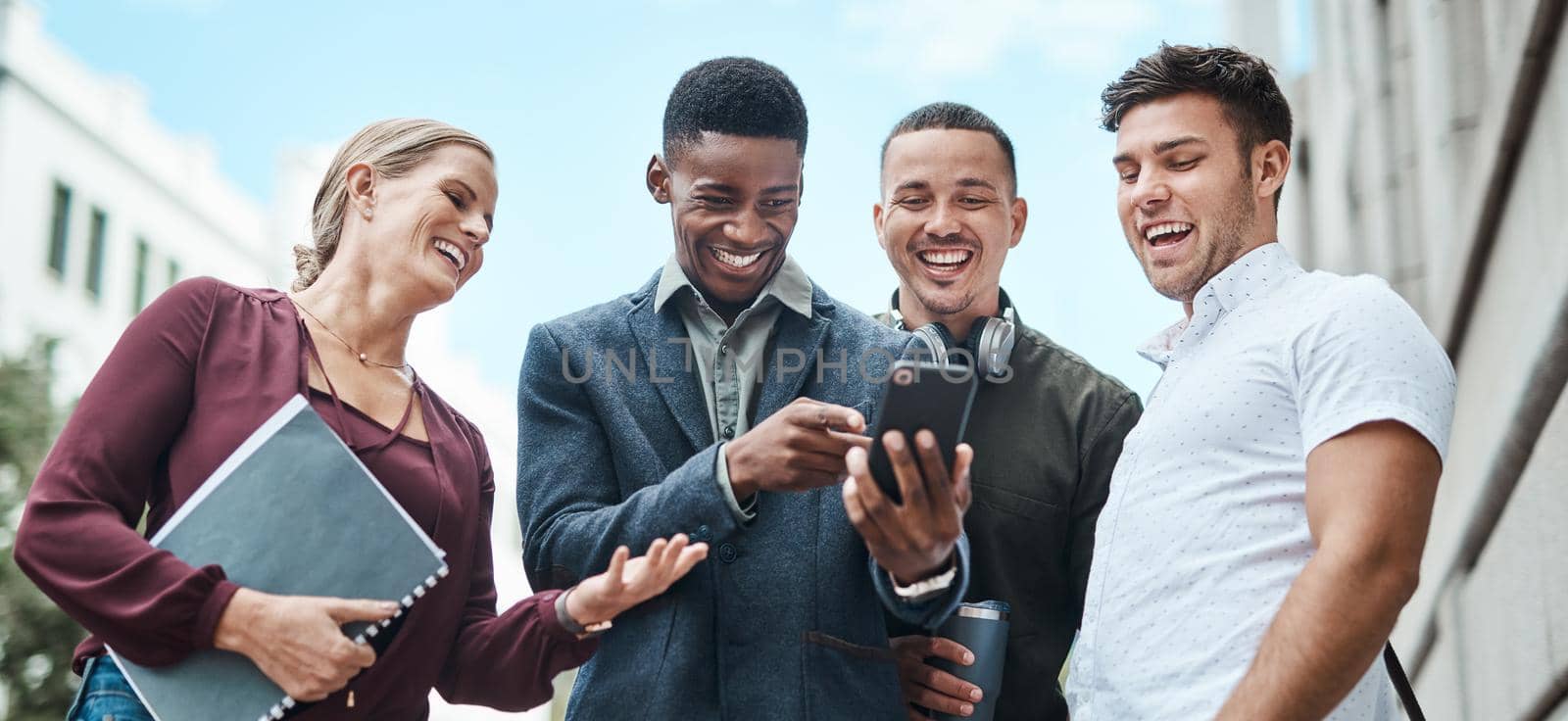 No office, no problem. Shot of a group of businesspeople using a smartphone together against an urban background. by YuriArcurs