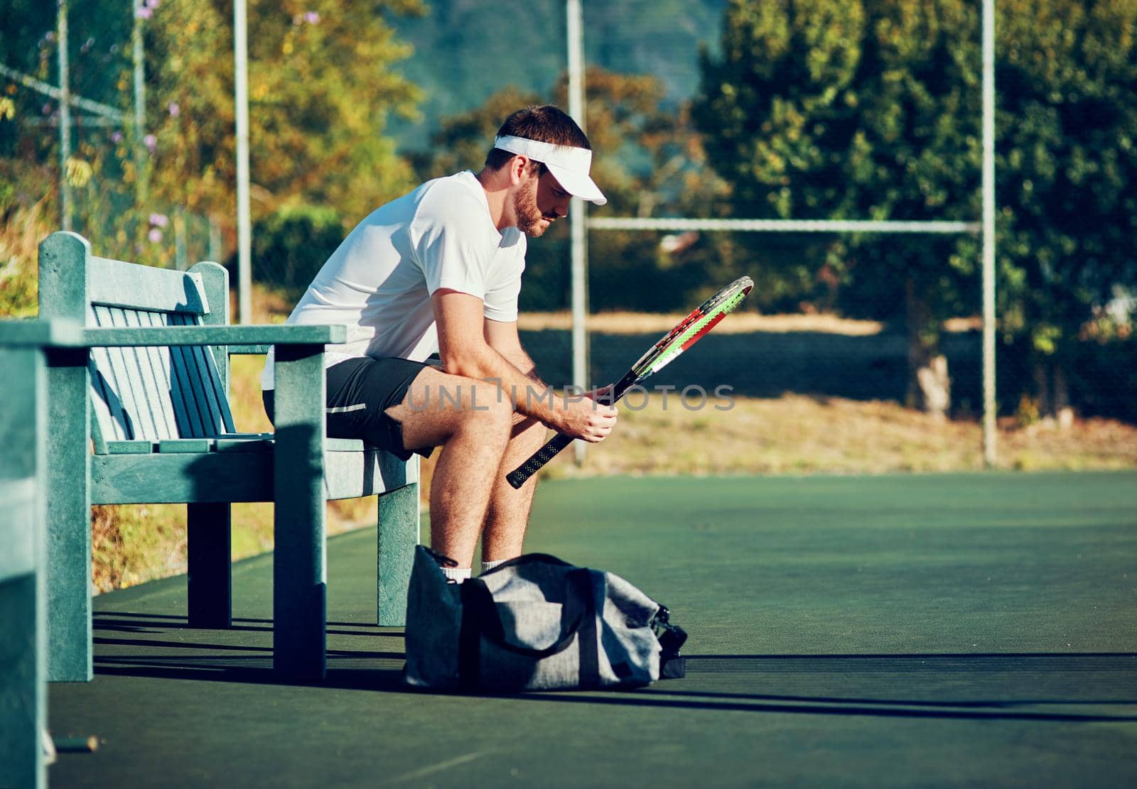 Shot of a sporty young man sitting on a bench on a tennis court