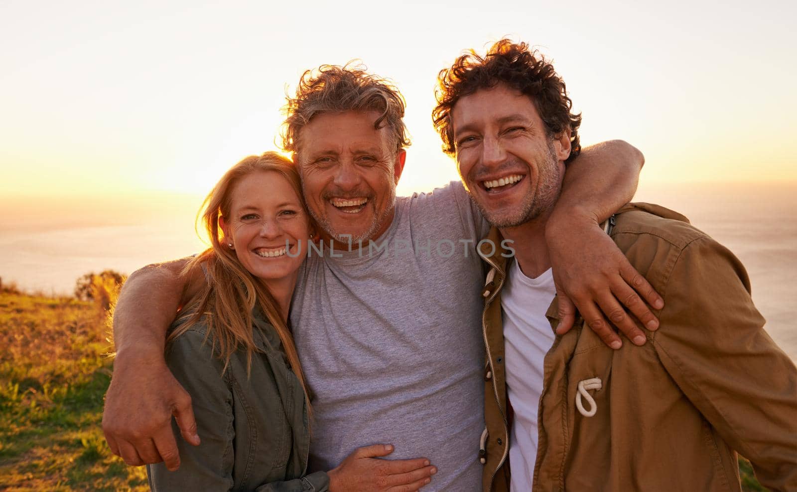 Portrait of a father with his son and daughter on a grassy hill at sunset