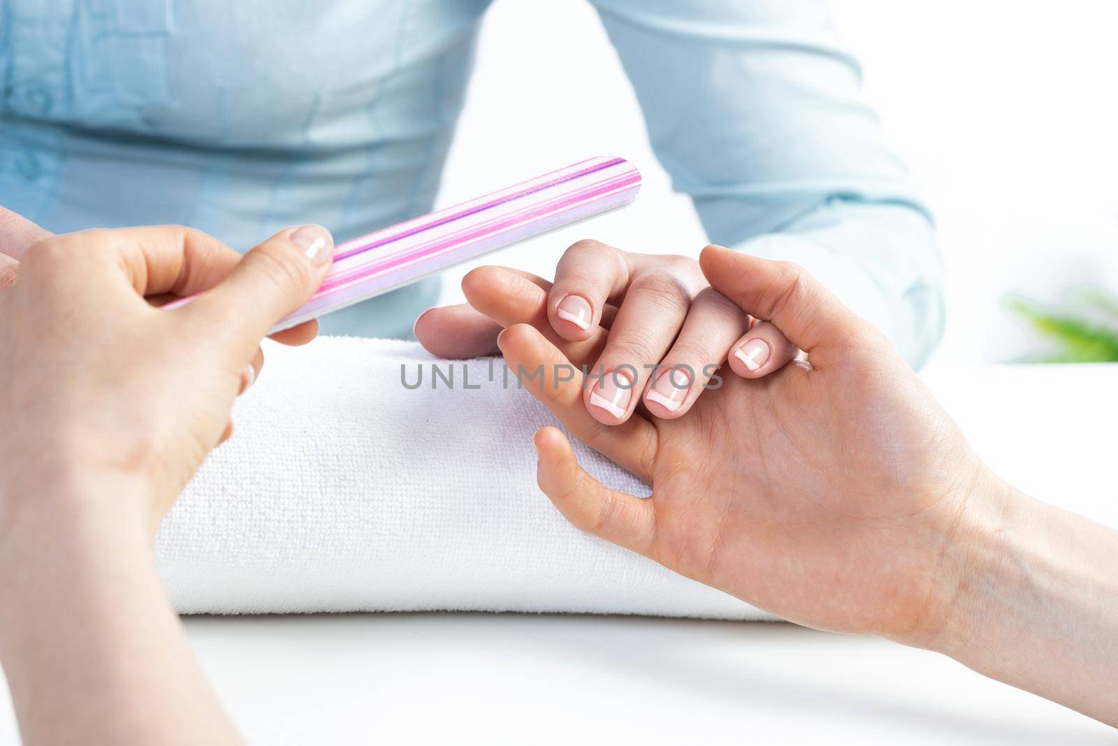 Manicurist using nail file and create perfect shape. Closeup of female hand preparing for apply nail polish. Beautician grinding nails with nail file tool. Professional nail care service.