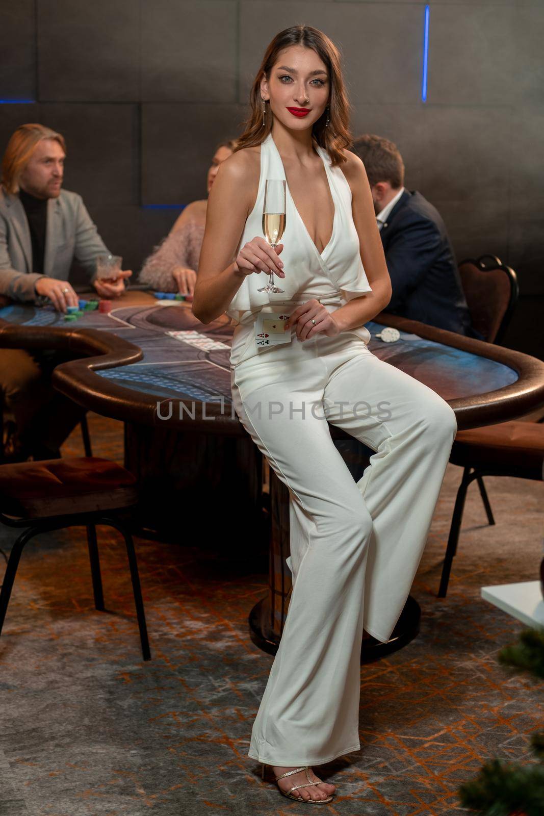 Smiling girl with pair of aces and glass of champagne sitting on gaming table by nazarovsergey