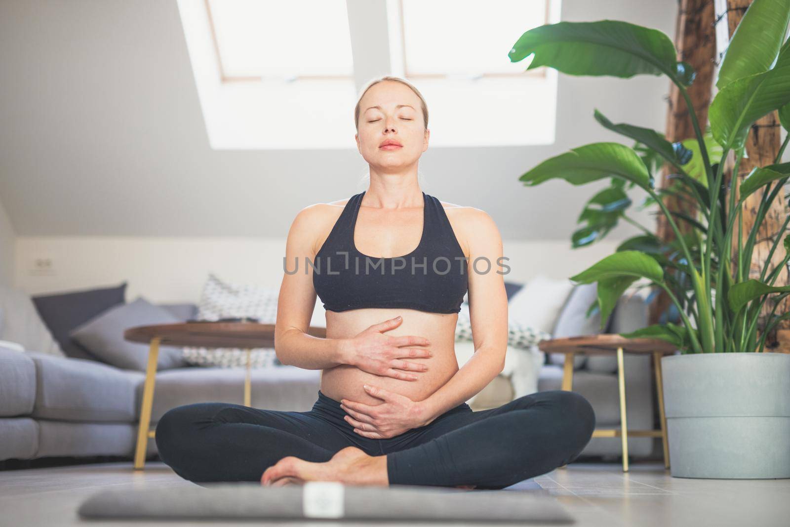 Young beautiful pregnant woman training yoga, caressing her belly. Young happy expectant relaxing, thinking about her baby and enjoying her future life. Motherhood, pregnancy, yoga concept