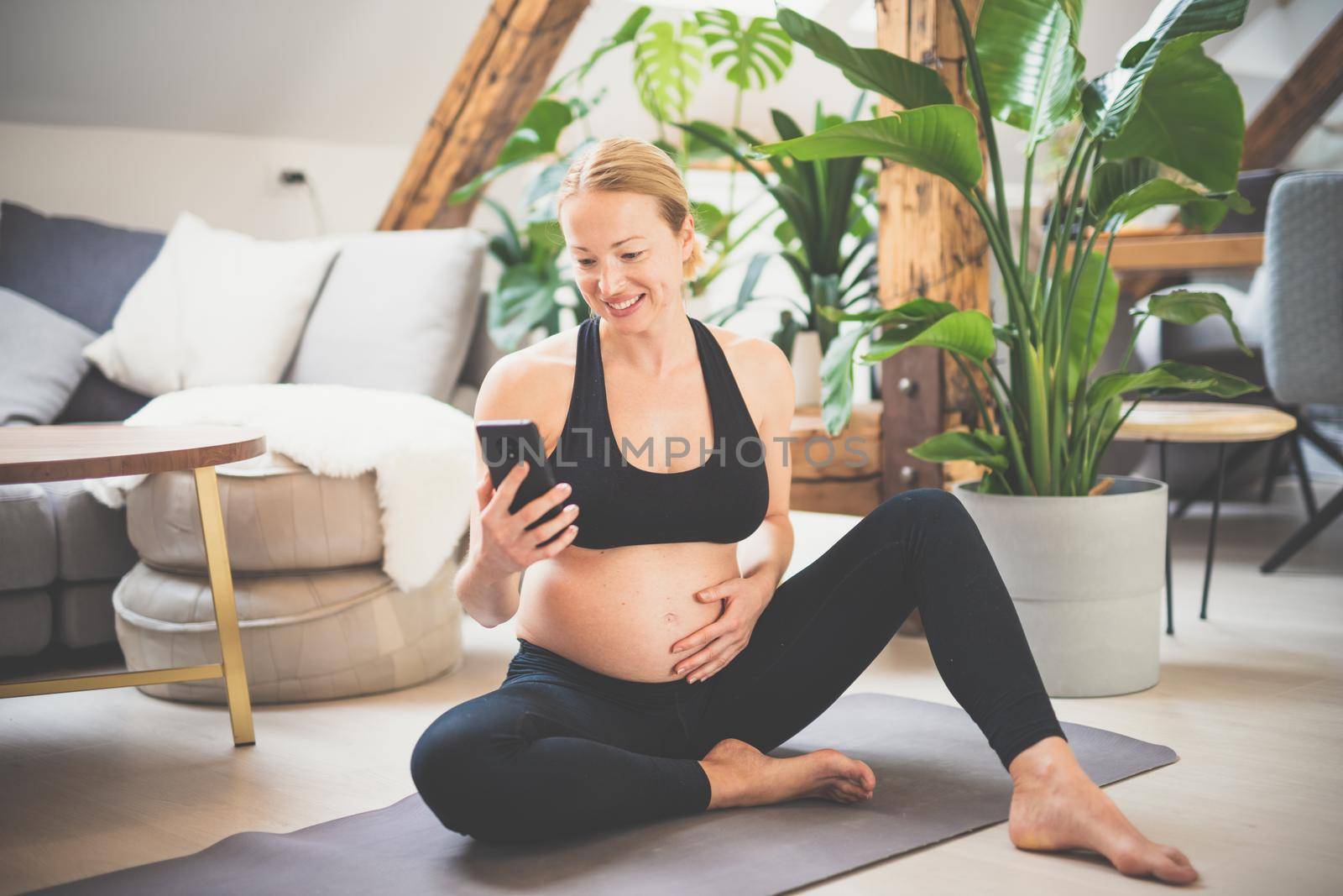 Young happy and cheerful beautiful pregnant woman chating to family and friends on mobile phone while staying fit, sporty and active on her maternity leave. Pregnancy, yoga concept by kasto