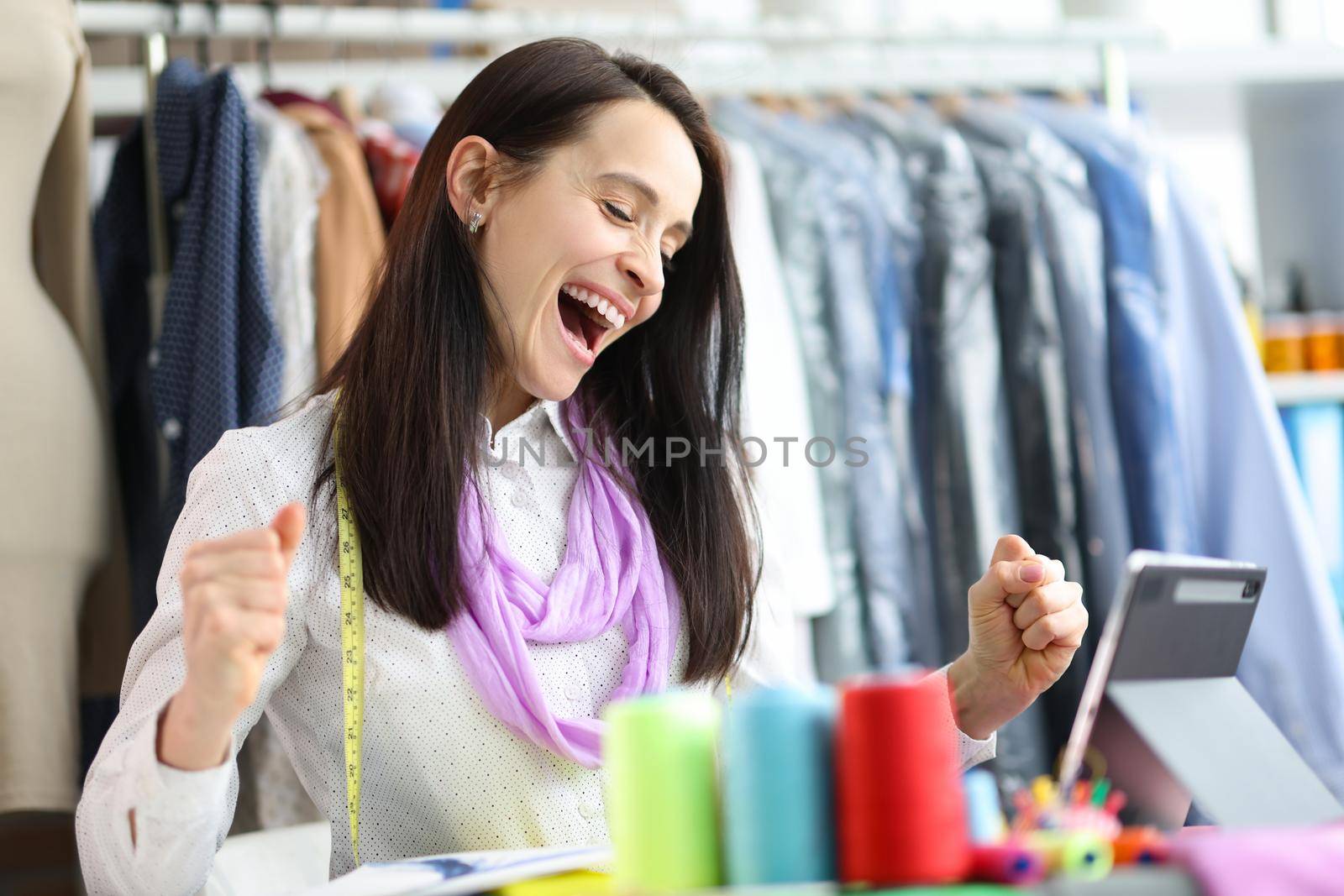 Joyful happy woman seamstress stylist at workplace. Successful fashion collection concept