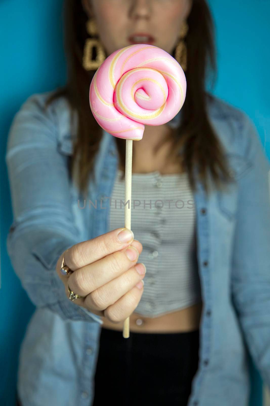Happy beautiful woman giving colorful pink twirl lollipop on light blue background. Sweets,hard candy,gift,present concept by Annebel146