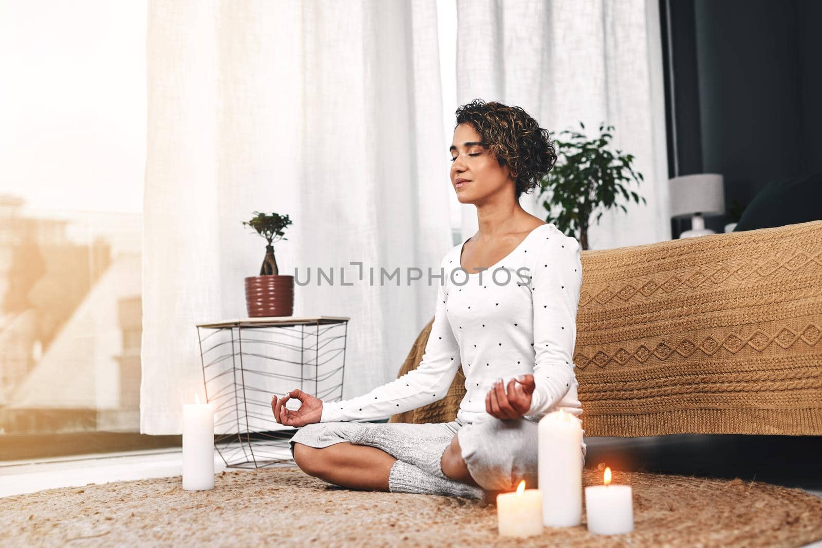 Scented candles help me relax. Full length shot of an attractive young woman sitting and meditating with candles in her living room at home. by YuriArcurs