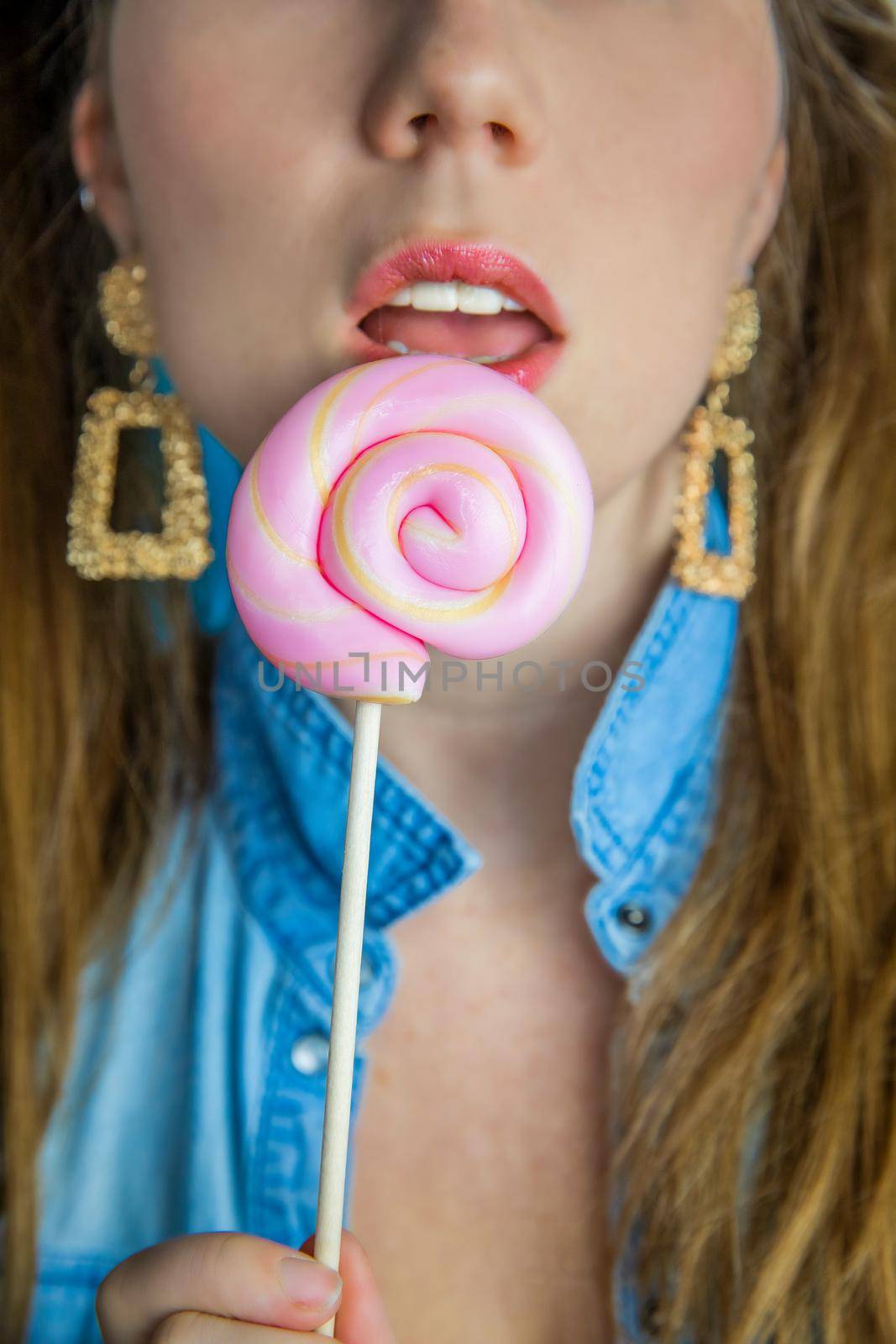 Portrait of a beautiful girl with colorful pink twirl lollipop hard candy on blue background, sweets,sugar and unhealthy food concept beauty