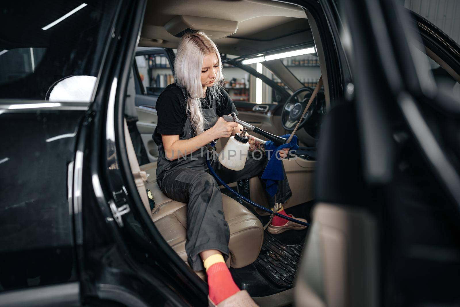 Woman cleaning car salon with polishing spray in car detailing service, close up