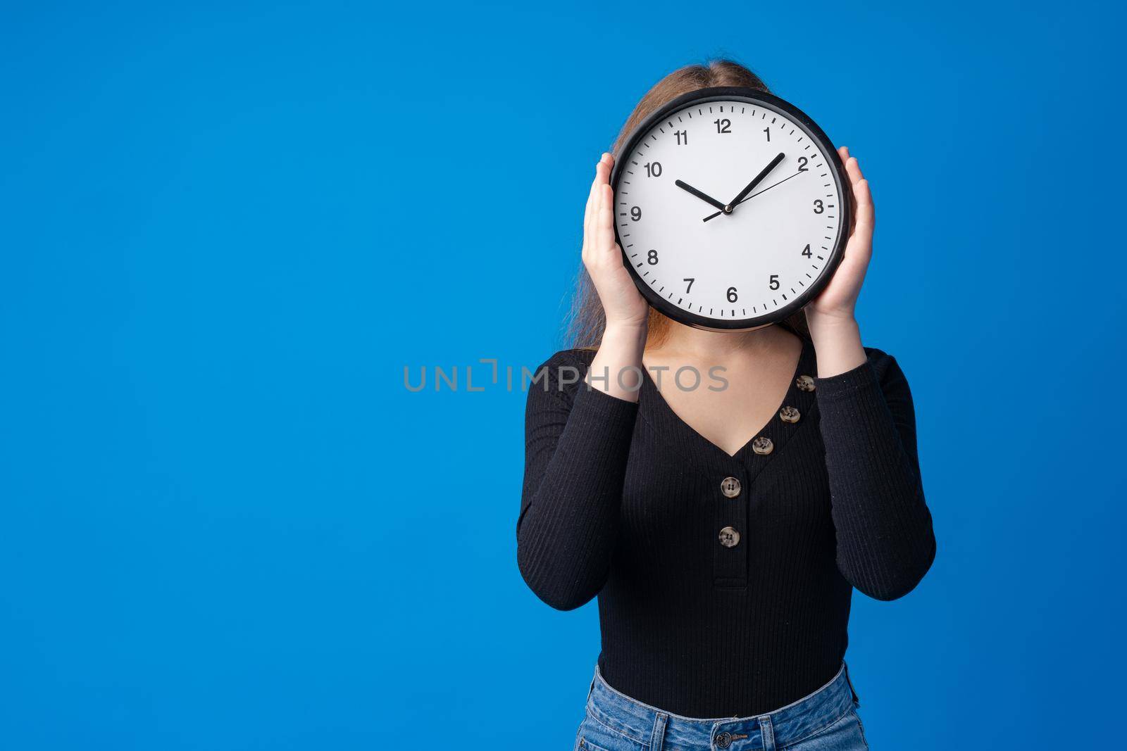 Beautiful teen girl holding wall clock over blue background, close up