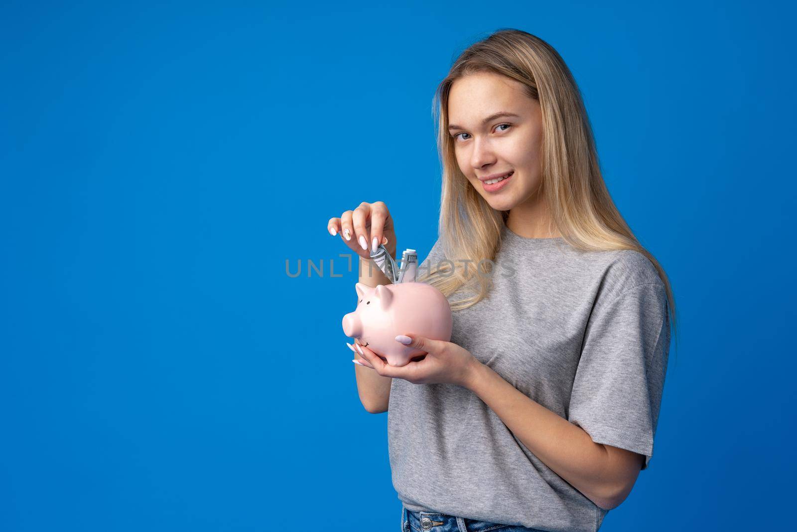 Teen girl with piggy bank on blue background, close up