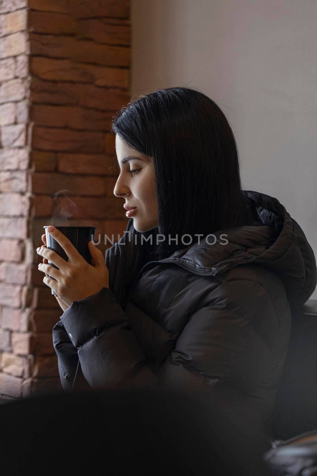 brunette girl in a down jacket sits in a cafe and drinks tea by but_photo