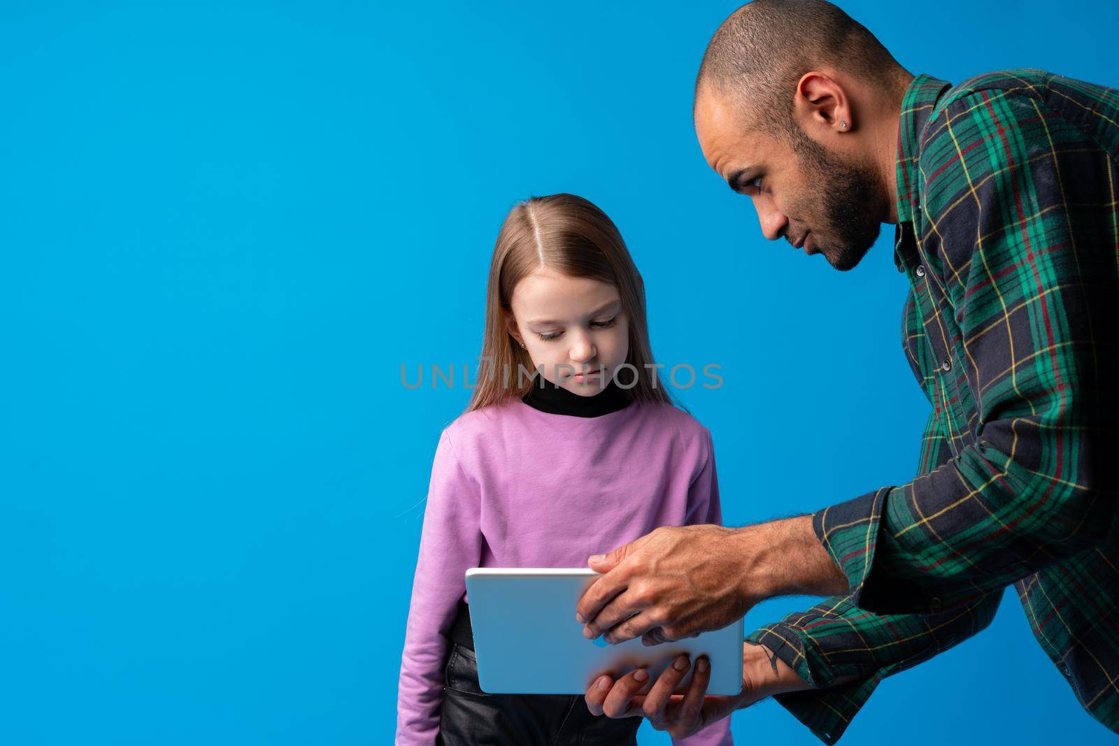 School teacher talking to pupil using digital tablet on blue background in studio