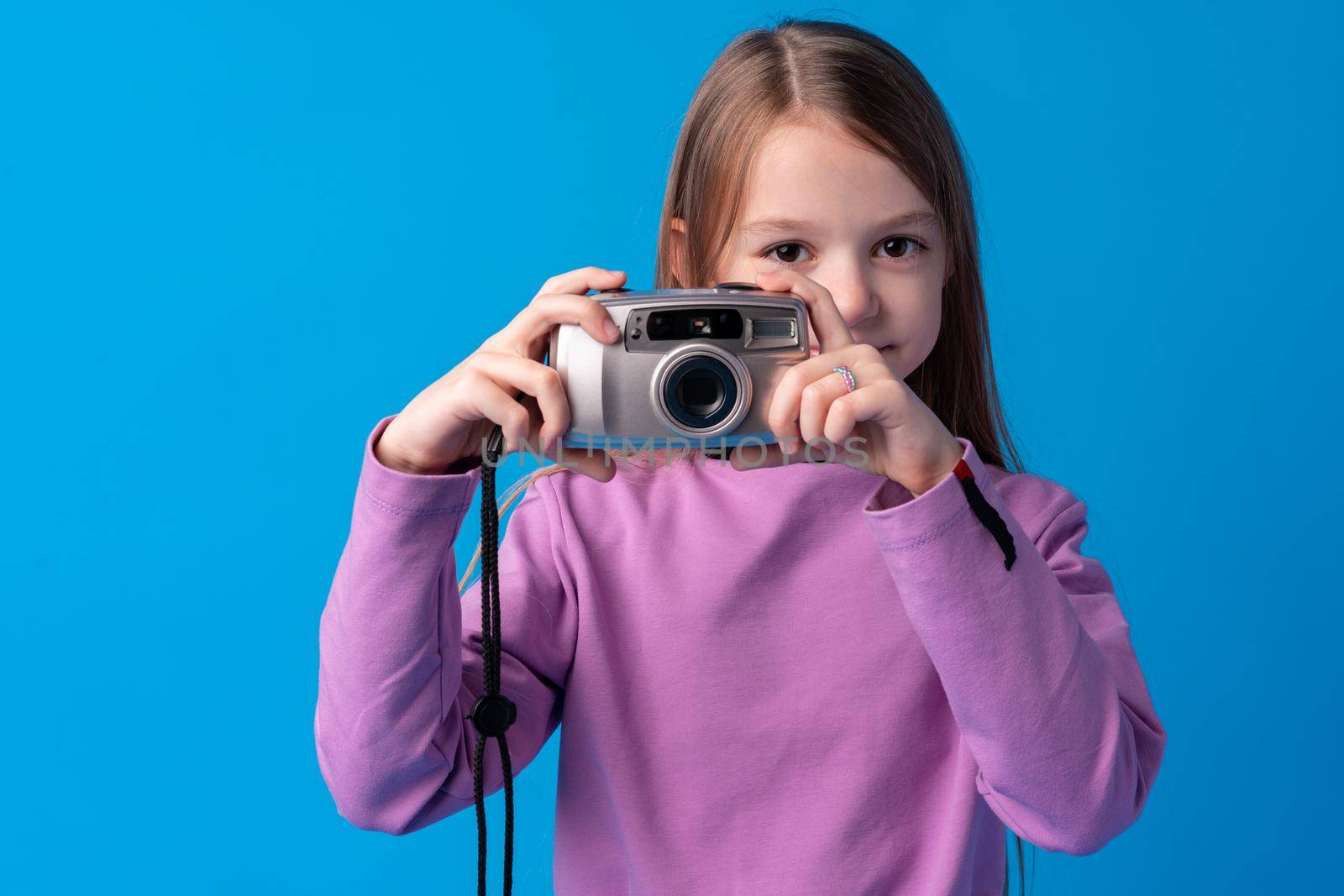 Portrait of a little girl with camera against blue background, close up