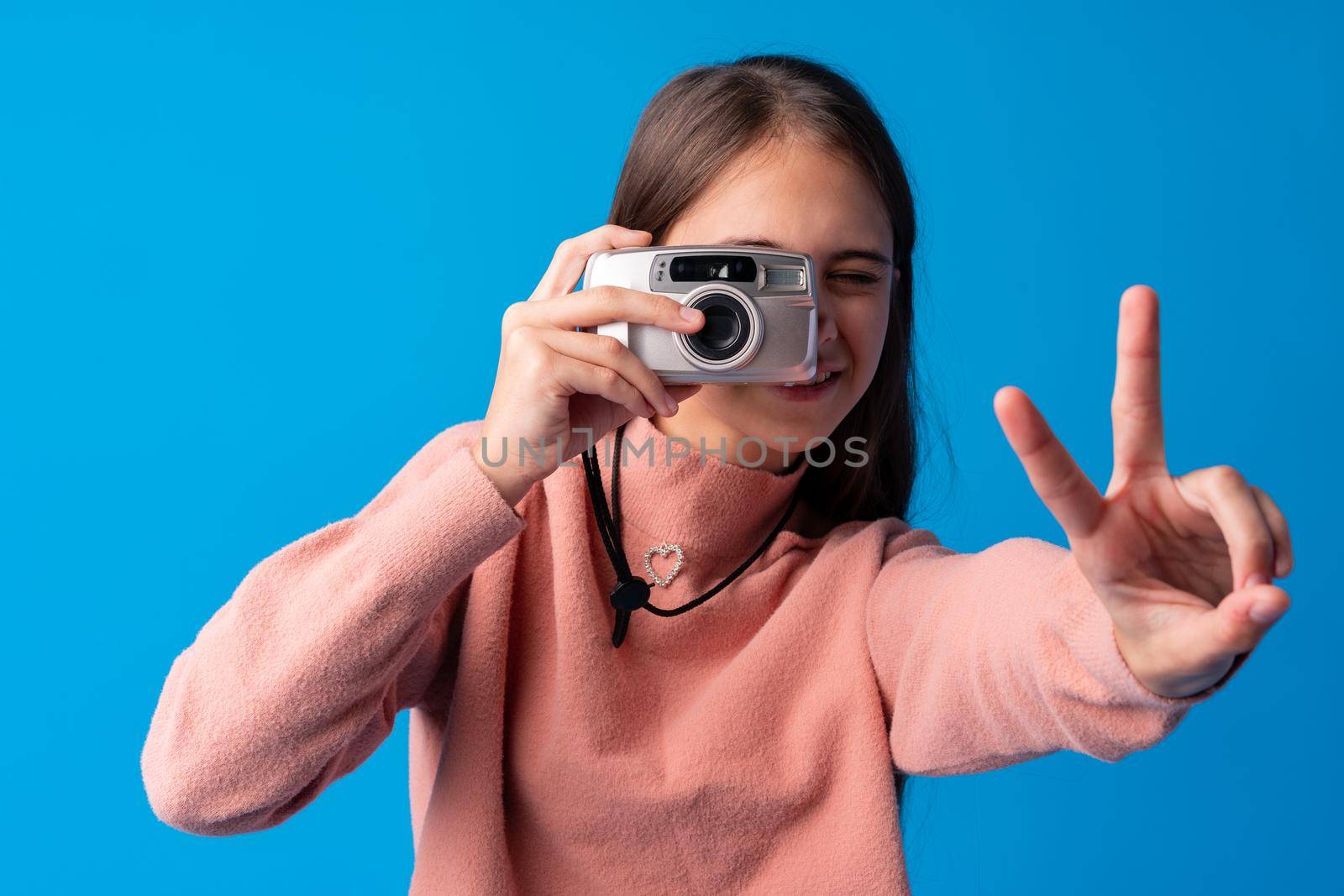 Portrait of a little girl with camera against blue background, close up