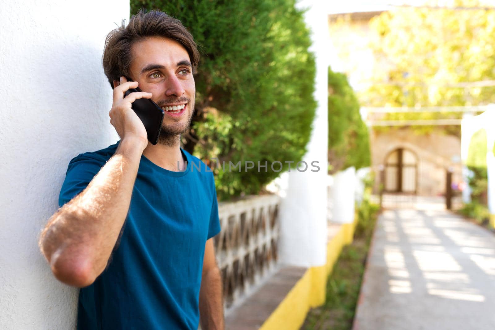 Young caucasian man talking on mobile phone in a park outdoors.Copy space. by Hoverstock