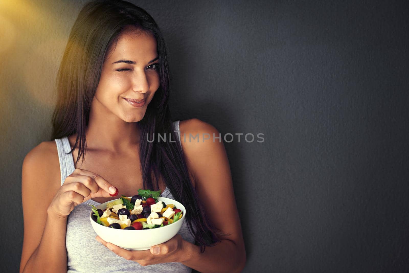 You're gonna love this. Portrait of a healthy young woman eating a salad against a gray background. by YuriArcurs