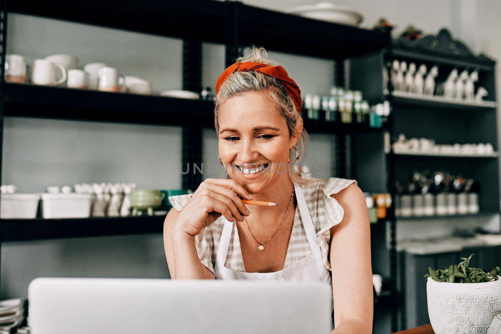 Cropped shot of an attractive mature woman sitting alone and using her laptop in her pottery workshop