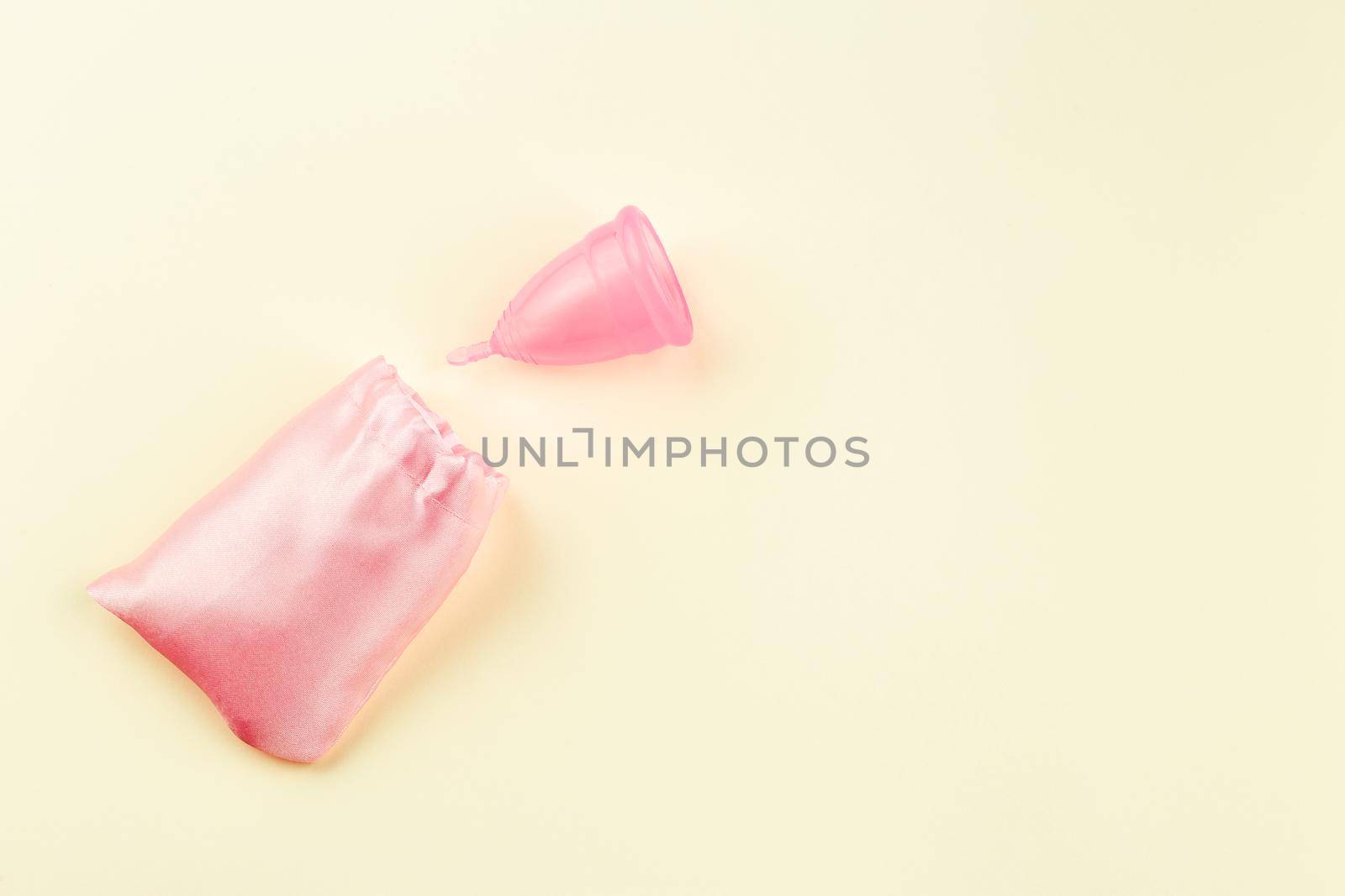 Pink Silicone Menstrual Cup near pink Storage Cloth Bag over beige Background. Space for Text, Top View. Women Sanitary Tool for Comfortable and Sustainable Periods