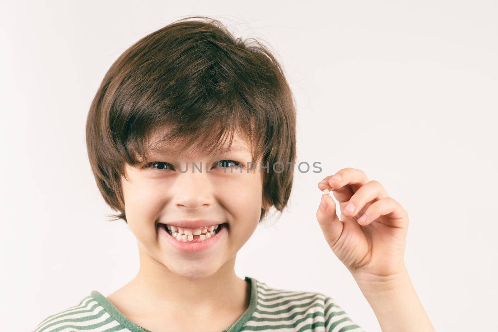 Young toothless boy demonstrates his first lost bottom front milk tooth over grey background. Child dental health care concept. Boy is smiling and looking into the camera