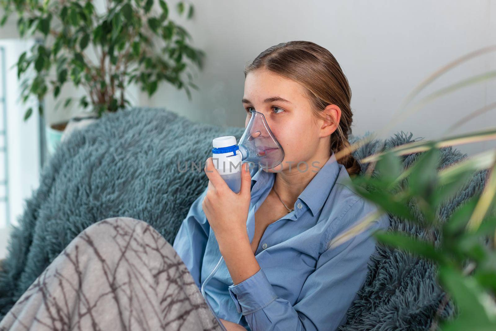 Teenage girl makes inhalation with a nebulizer equipment. Sick child holding inhalator in hand and breathes through an inhaler at home. Physical therapy for cold, flu and bronchial asthma