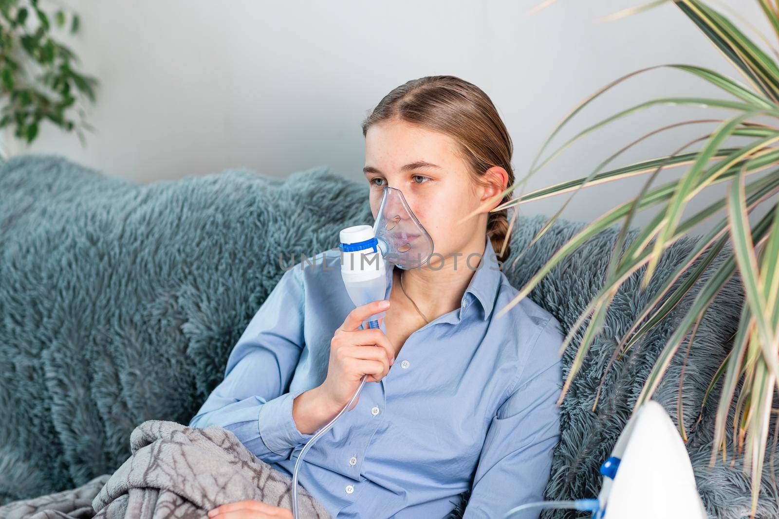 Teenage girl makes inhalation with a nebulizer equipment. Sick child holding inhalator in hand and breathes through an inhaler at home. Physical therapy for cold, flu and bronchial asthma