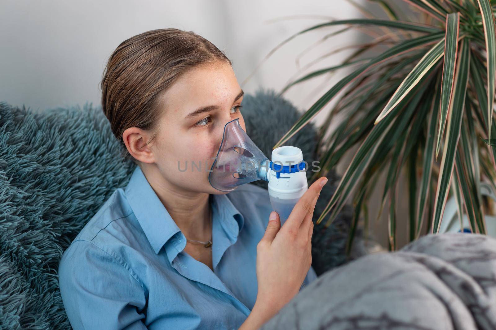 Teenage girl makes inhalation with a nebulizer equipment. Sick child holding inhalator in hand and breathes through an inhaler at home. Physical therapy for cold, flu and bronchial asthma