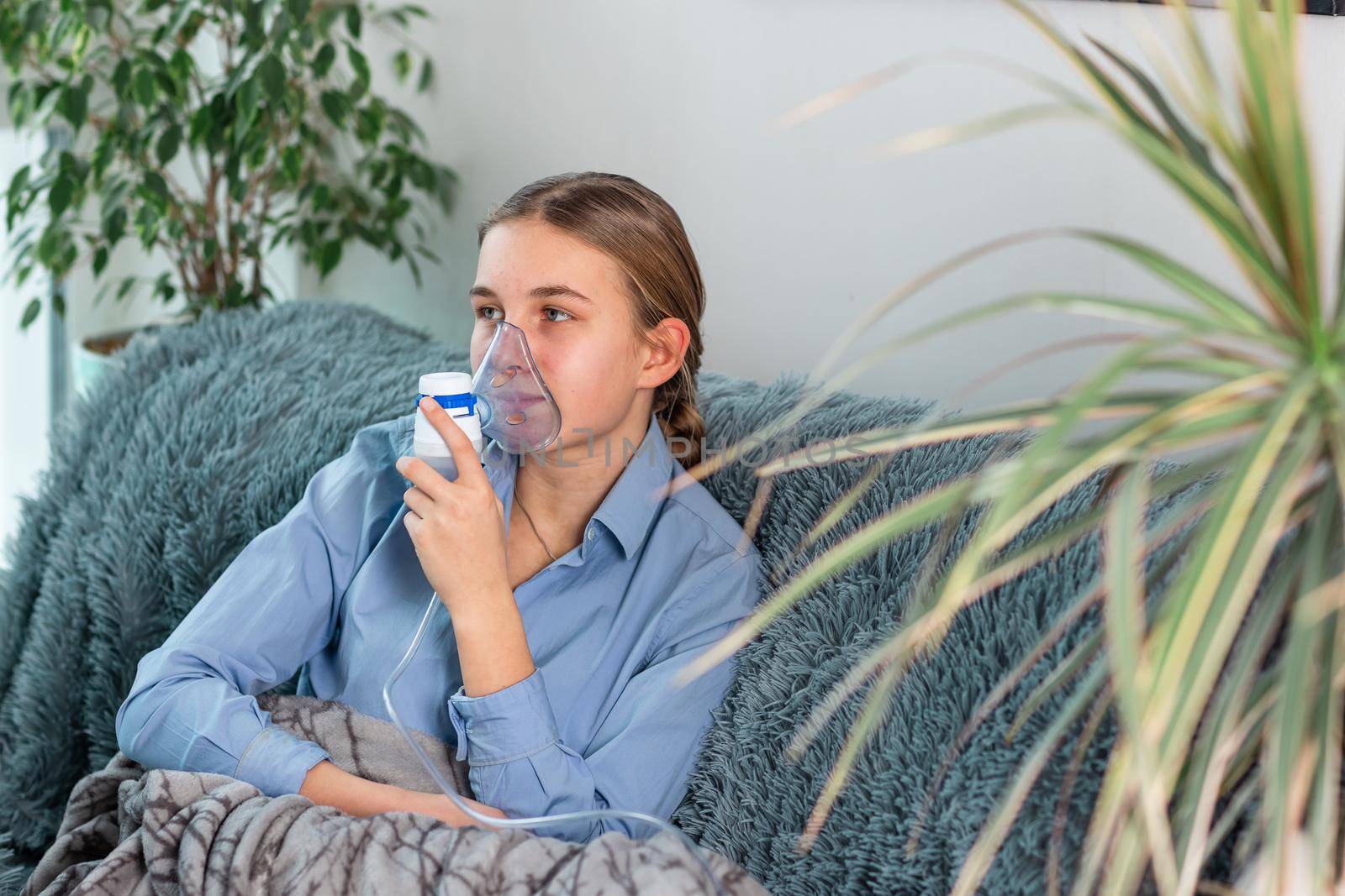 Teenage girl makes inhalation with a nebulizer equipment. Sick child holding inhalator in hand and breathes through an inhaler at home by Len44ik