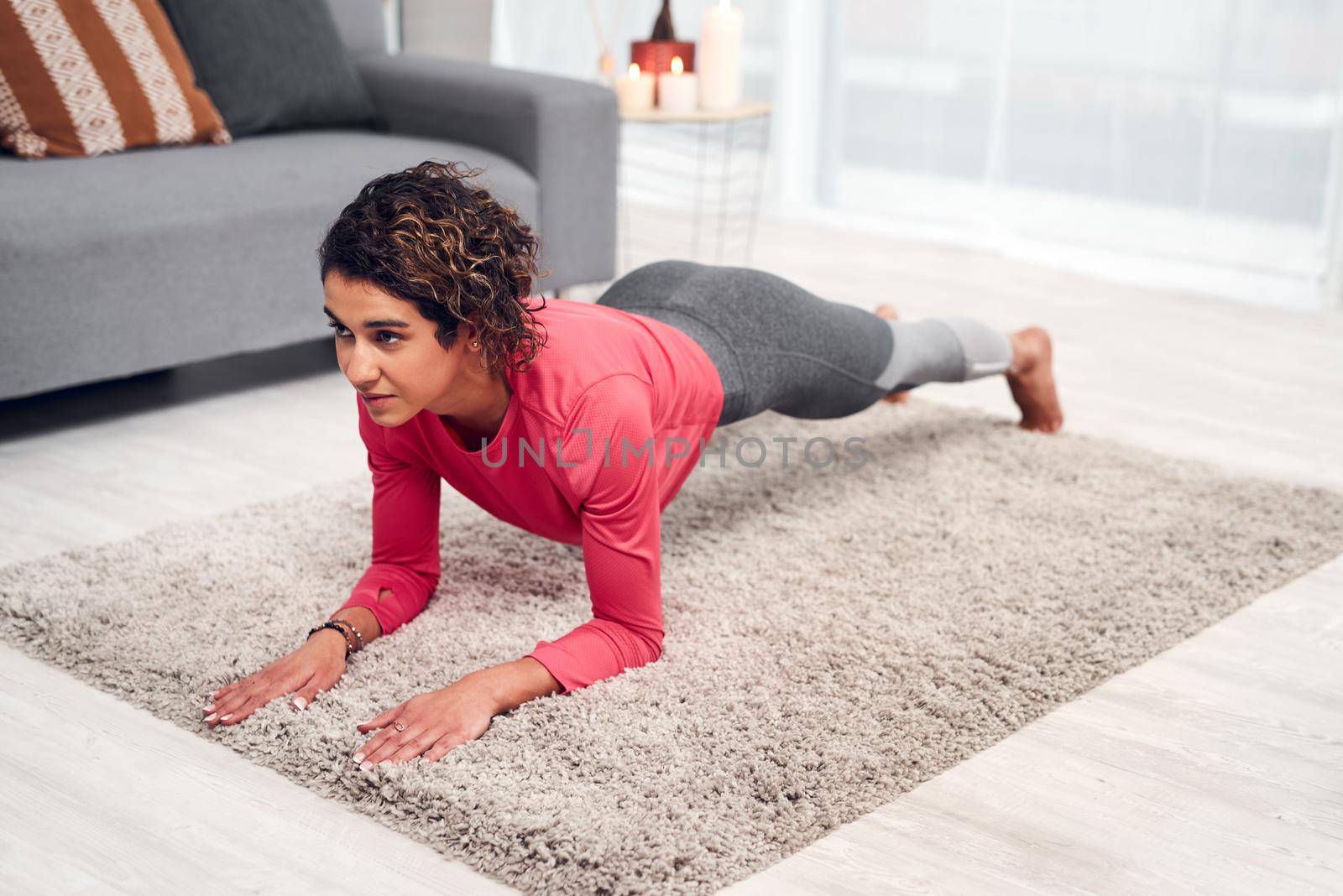 Feel the burn. Full length shot of an attractive young woman exercising and holding a plank while in her living room at home. by YuriArcurs