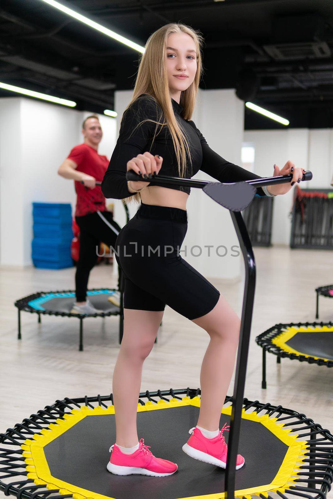Beautiful girl on a yellow trampoline, in red sneakers stands in the gym. Women's and men's group on a sports trampoline, fitness training, healthy life - a concept trampoline group batut instructor men, from female athletic in sporty and sport motion, shape sportswear. Legs beauty athlete by 89167702191