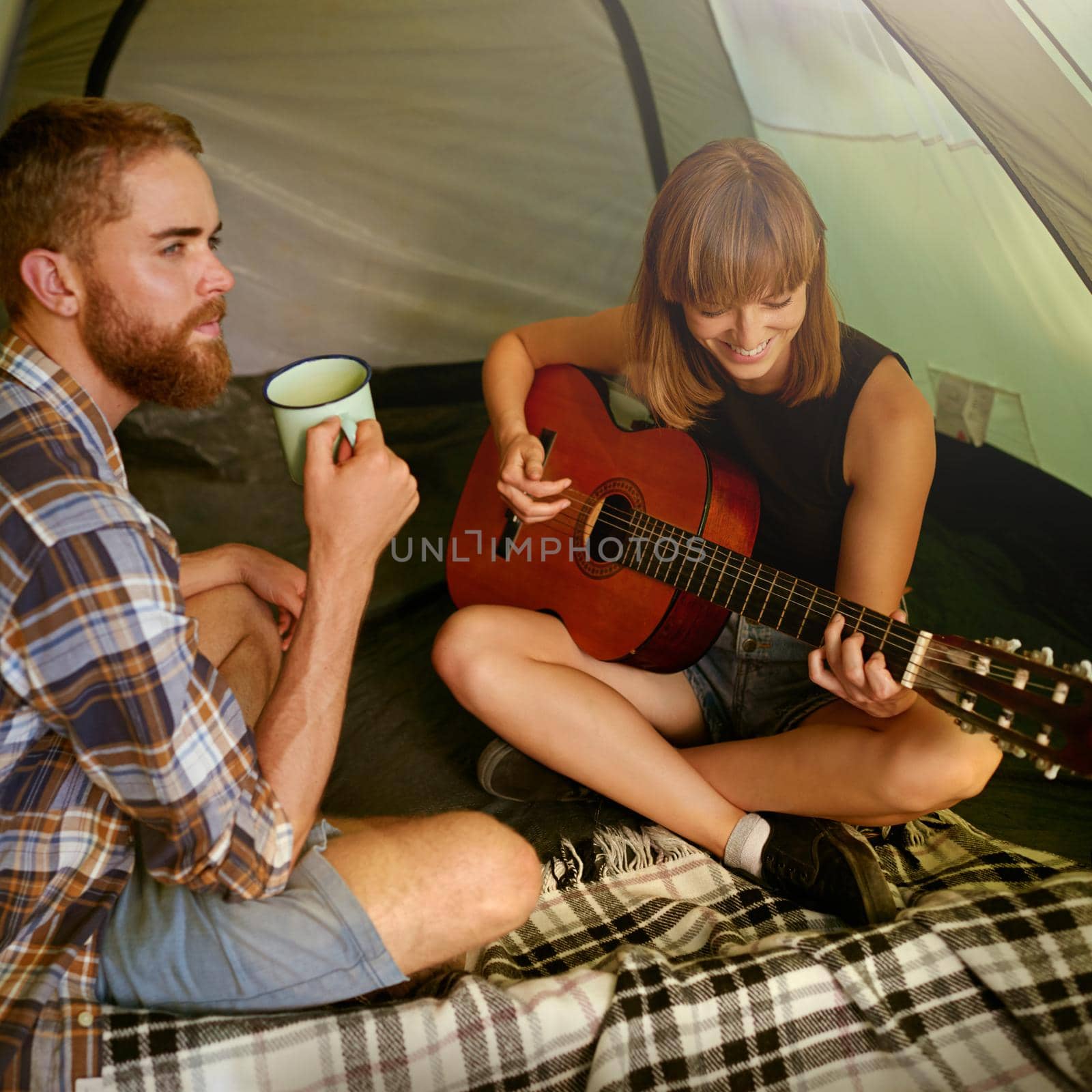 They always bring the music. Shot of a young woman playing guitar to her boyfriend in a tent. by YuriArcurs