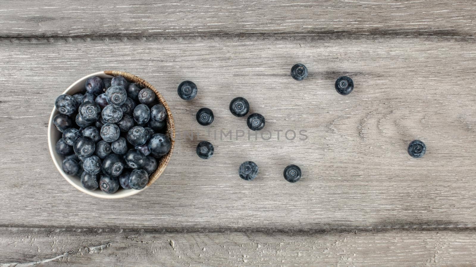 Table top view - small bowl of blueberries, some of them spilled on rustic desk.