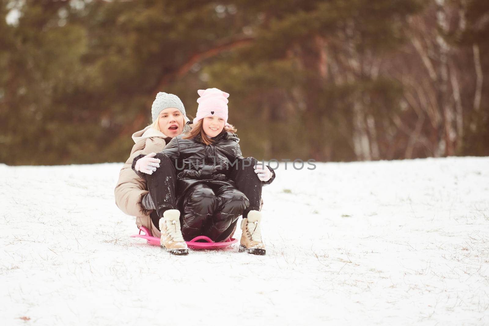 Happy mother with baby girl sitting on sledge and sledding down on snow from hill. Enjoying white winter day at park. Spending time together in weekend. by sarymsakov
