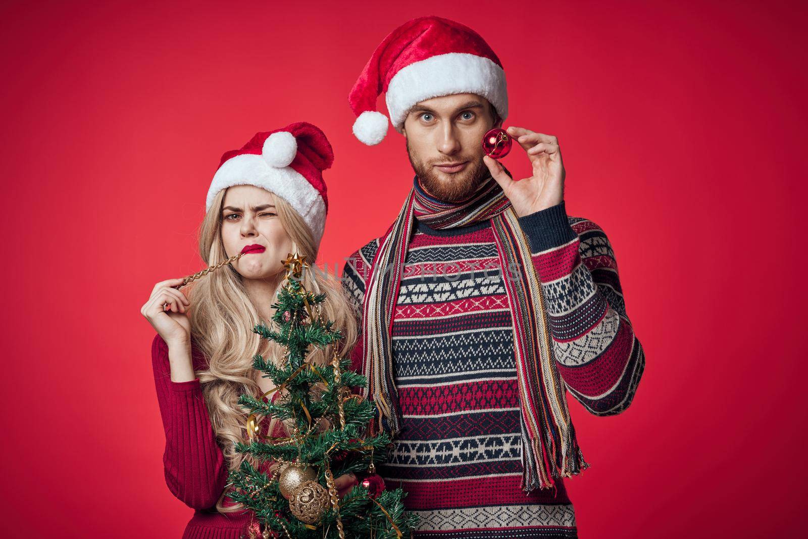 cute young couple holding christmas tree toys decoration red background. High quality photo