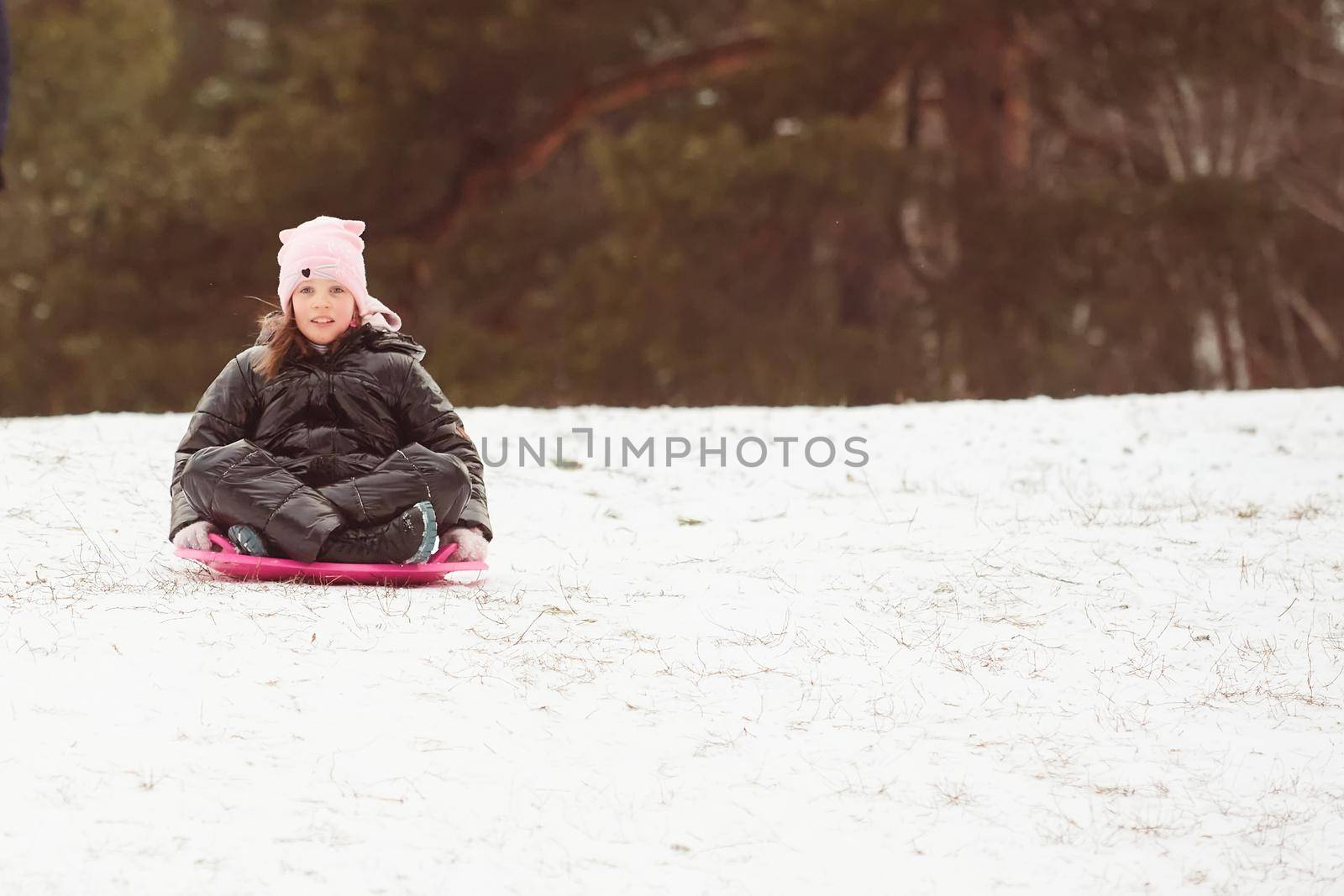Active girl sliding down the hill. Happy child having fun outdoors in winter on sledge. Family time. by sarymsakov
