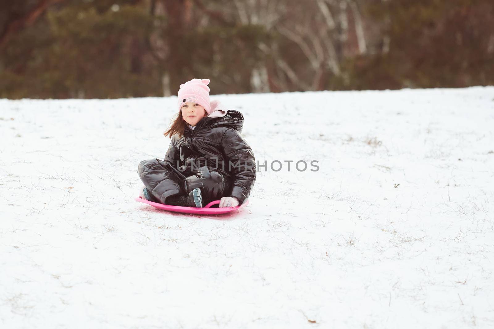 Happy little girl sliding down the hill on saucer sled. Girl enjoying slider ride on the snow.