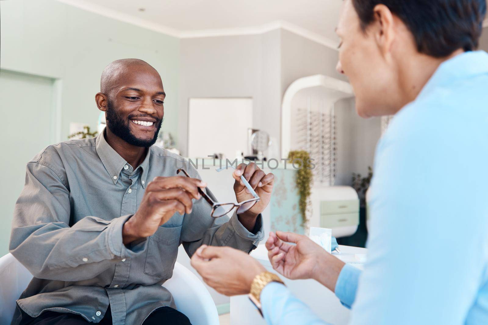 Shot of a an optometrist helping a young man choose a new pair of glasses