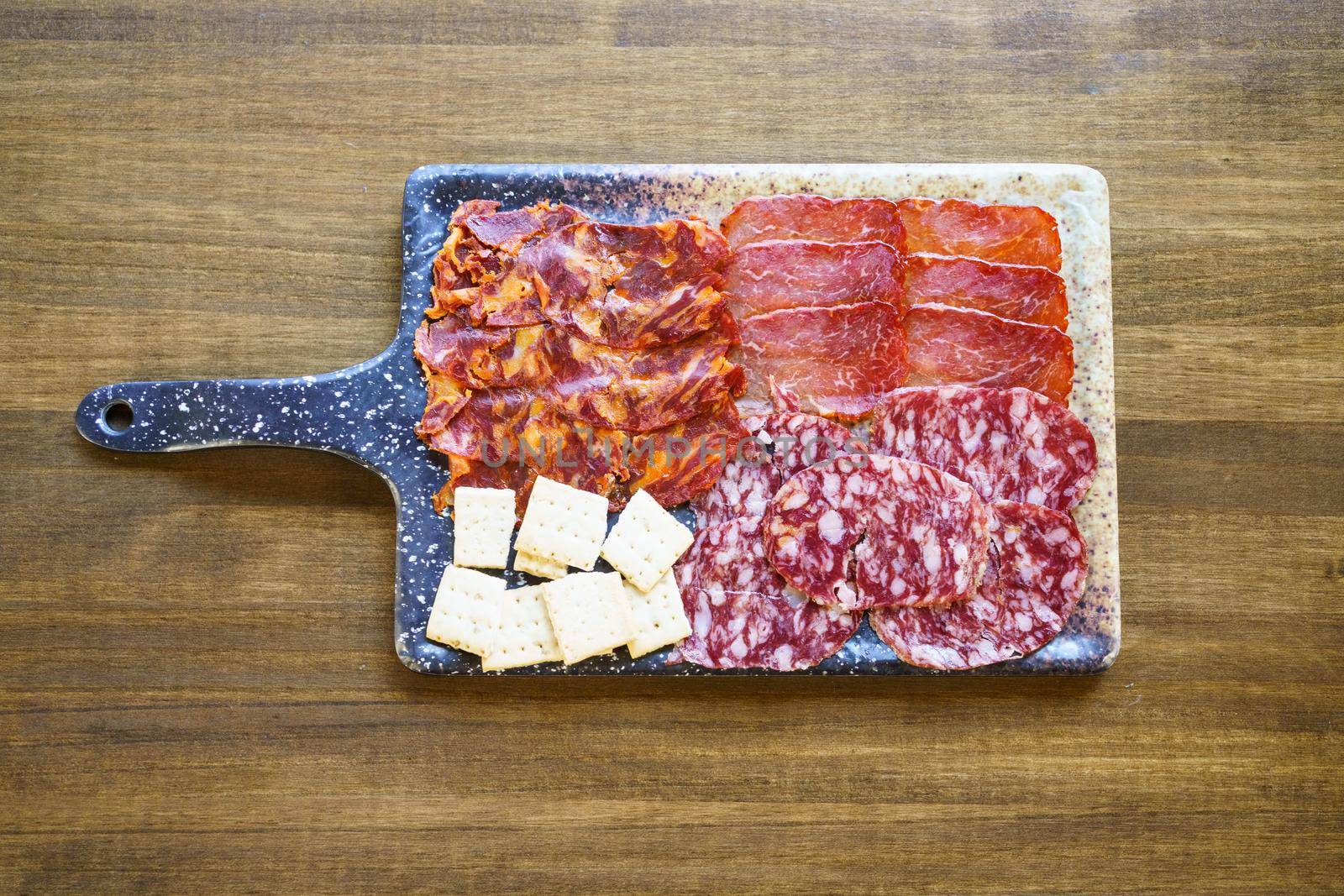 Top view of Iberian cured meats platter. A typical dish of Spanish cuisine. with crackers placed on board on lumber restaurant table