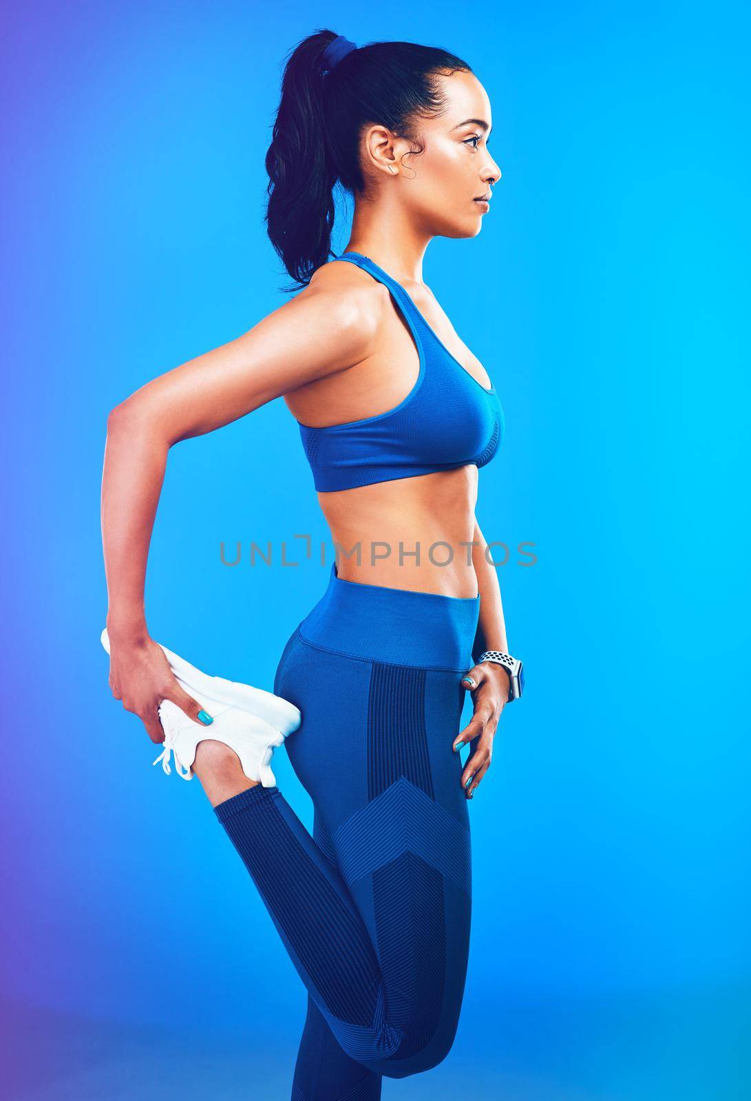 Studio shot of an attractive young sportswoman stretching her leg against a blue background