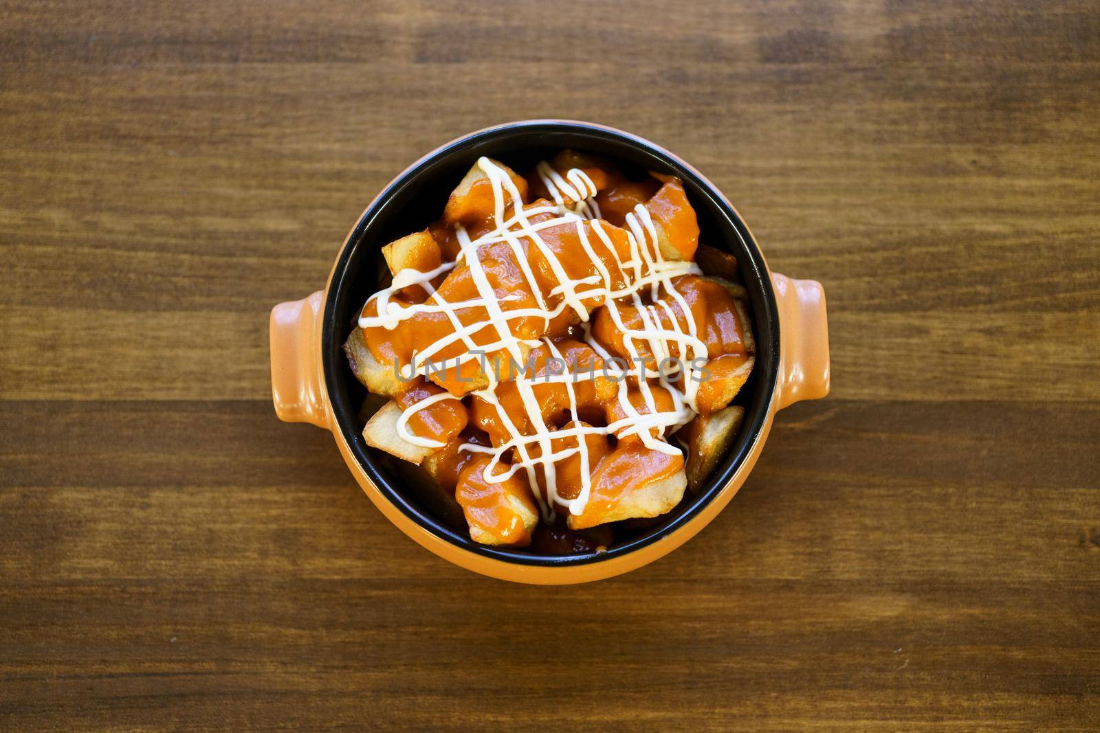 Top view of a delicious plate of patatas bravas, a typical Spanish dish, garnished with spicy sauce and served in a bowl on a wooden table in a restaurant.
