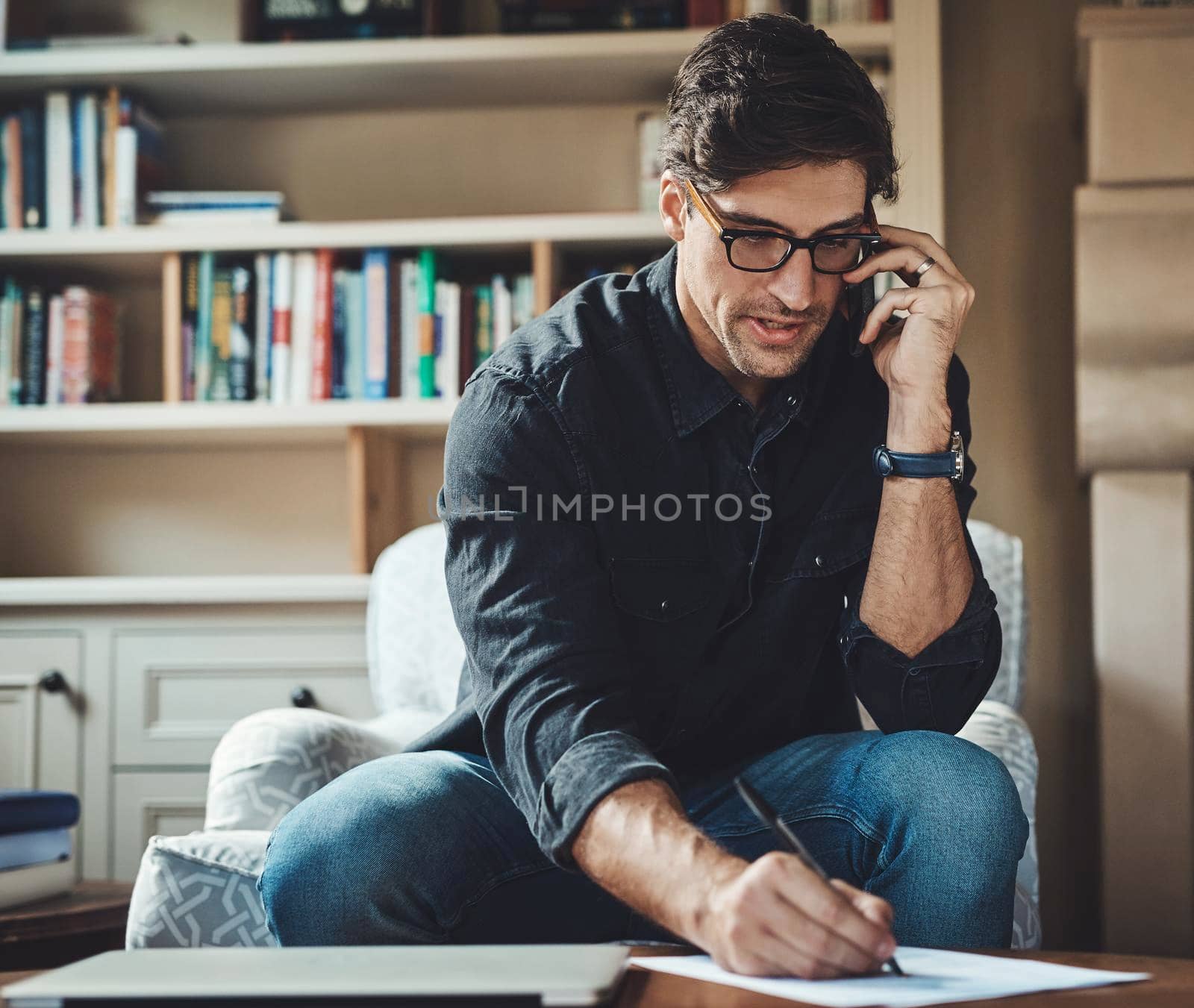Shot of a handsome young businessman making a phone call while working in his office at home