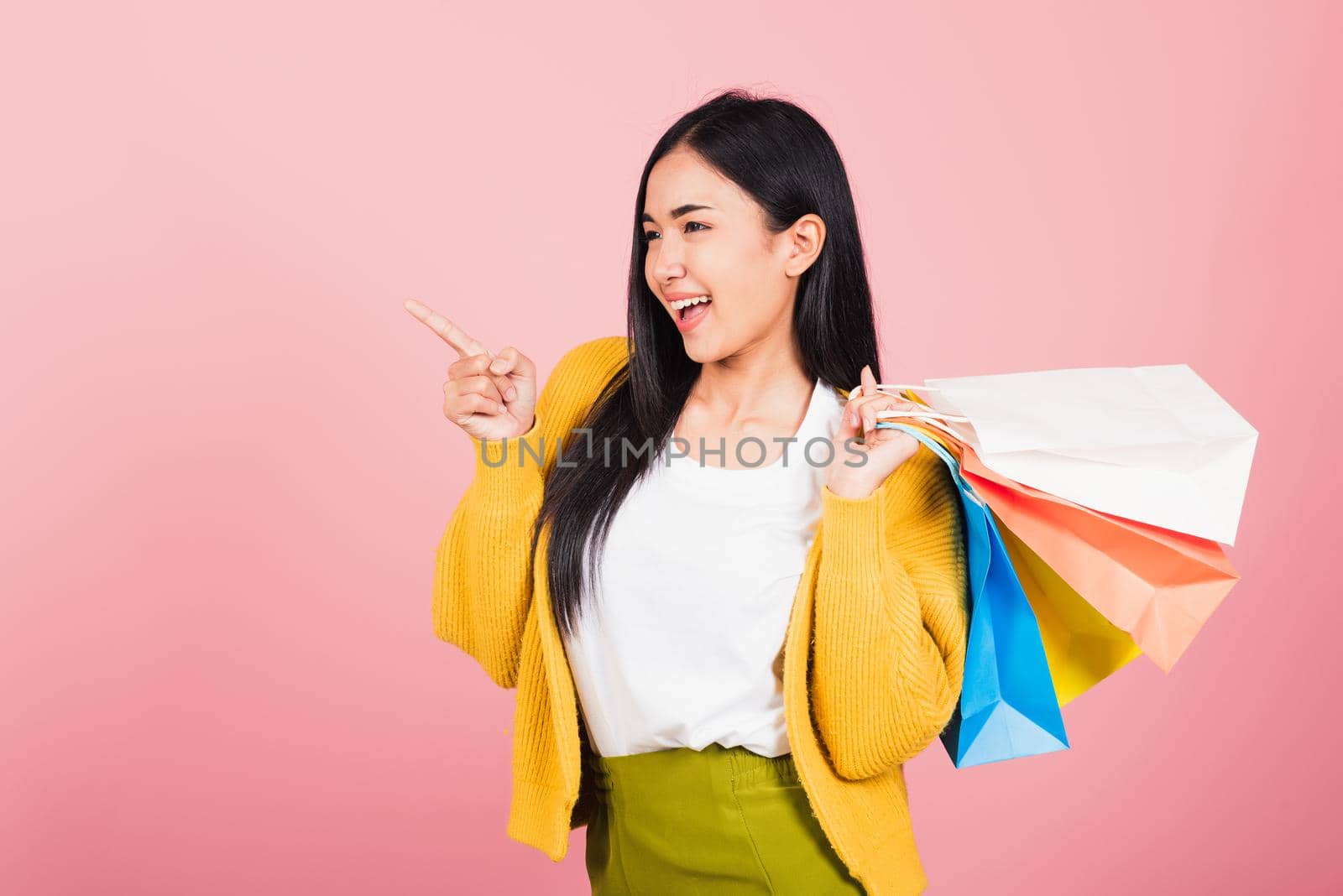 woman shopper smiling standing holding online shopping bags multicolor in summer pointing finger by Sorapop