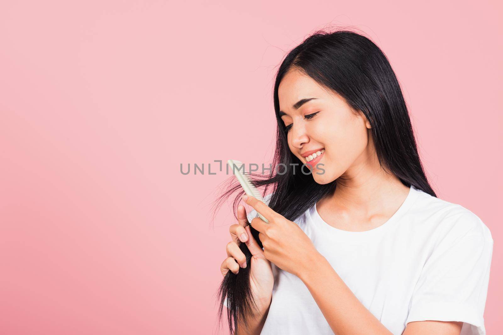 Portrait of Asian beautiful young woman smile combing her hair, happy female long healthy hair with hairbrush brushing hairs, studio shot isolated on pink background